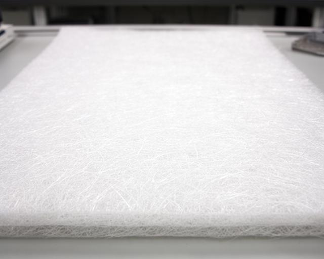 Manta de fibras cortadas de fibra de vidrio extendida sobre una mesa técnica, con superficie uniforme y blanca